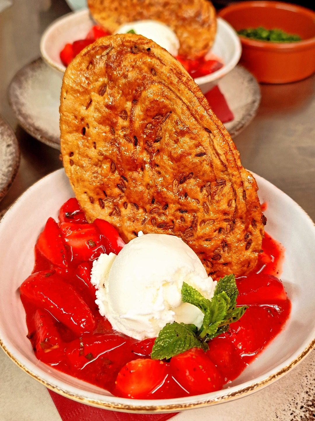Des fraises fraîches et une boule de glace sous une tuile croustillante, dans un bol à bord rouge