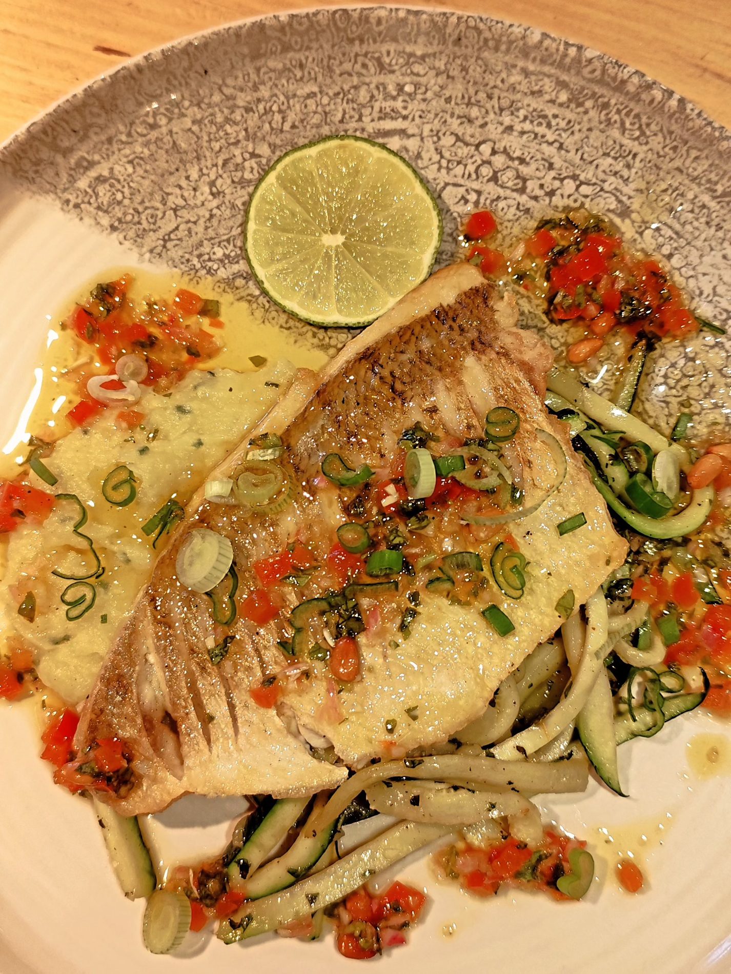 Un filet de poisson doré sur des légumes, relevé d'une rondelle de citron vert et d'une salsa de tomates